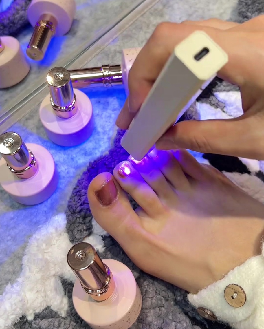 Une lampe UV/LED positionnée au-dessus dun orteil rose, la lumière violette illuminant longle lors de la catalyse.