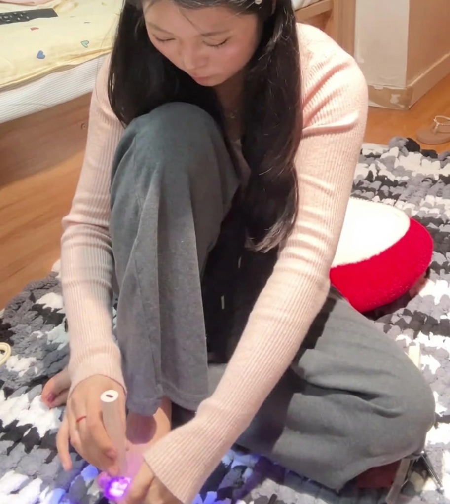 Une personne utilisant une lampe UV portable pour catalyser le gros orteil du pied gauche après application du vernis rose magnétique.