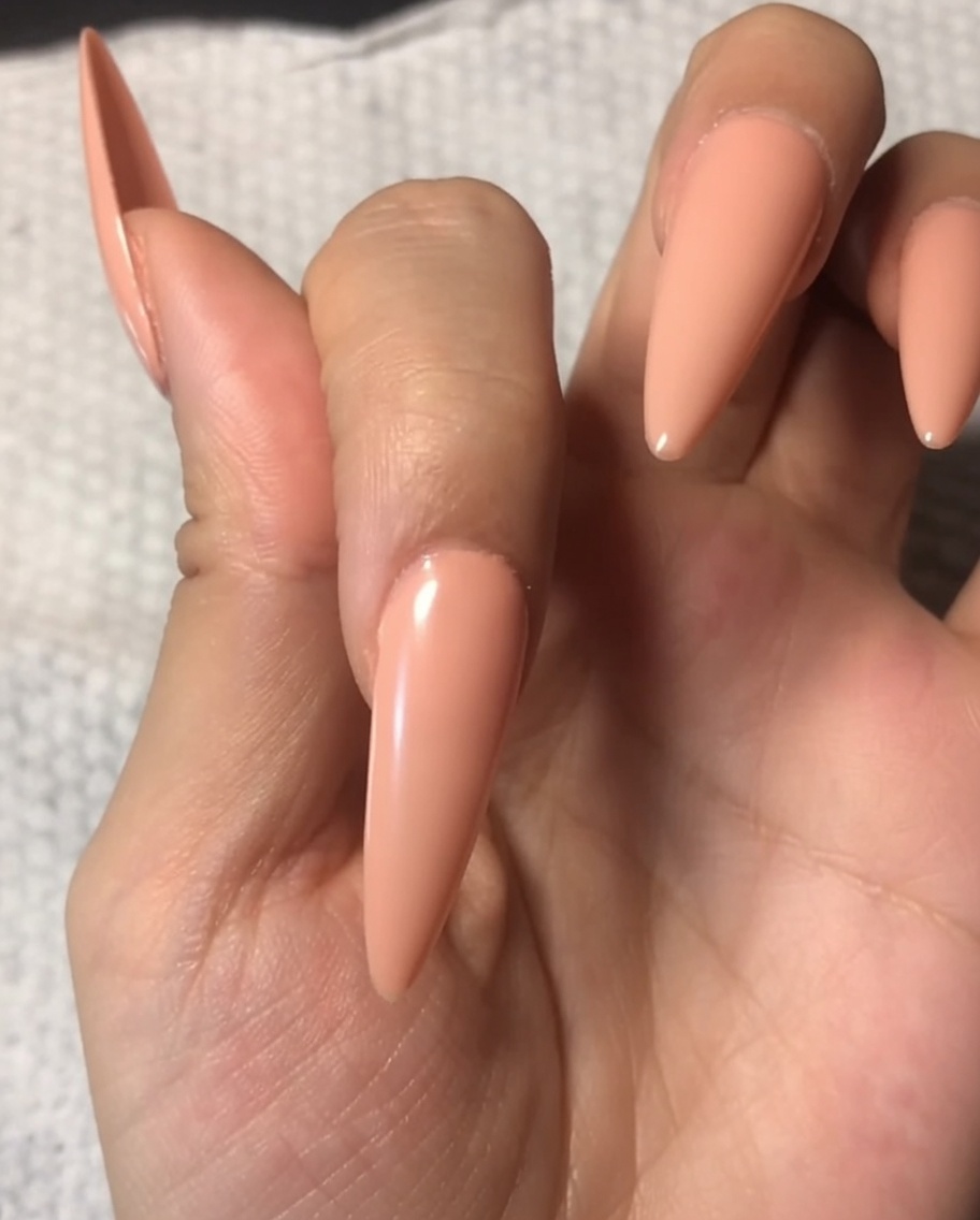 Un pinceau appliquant un top coat transparent et brillant sur un ongle déjà verni avec une base nude douce.