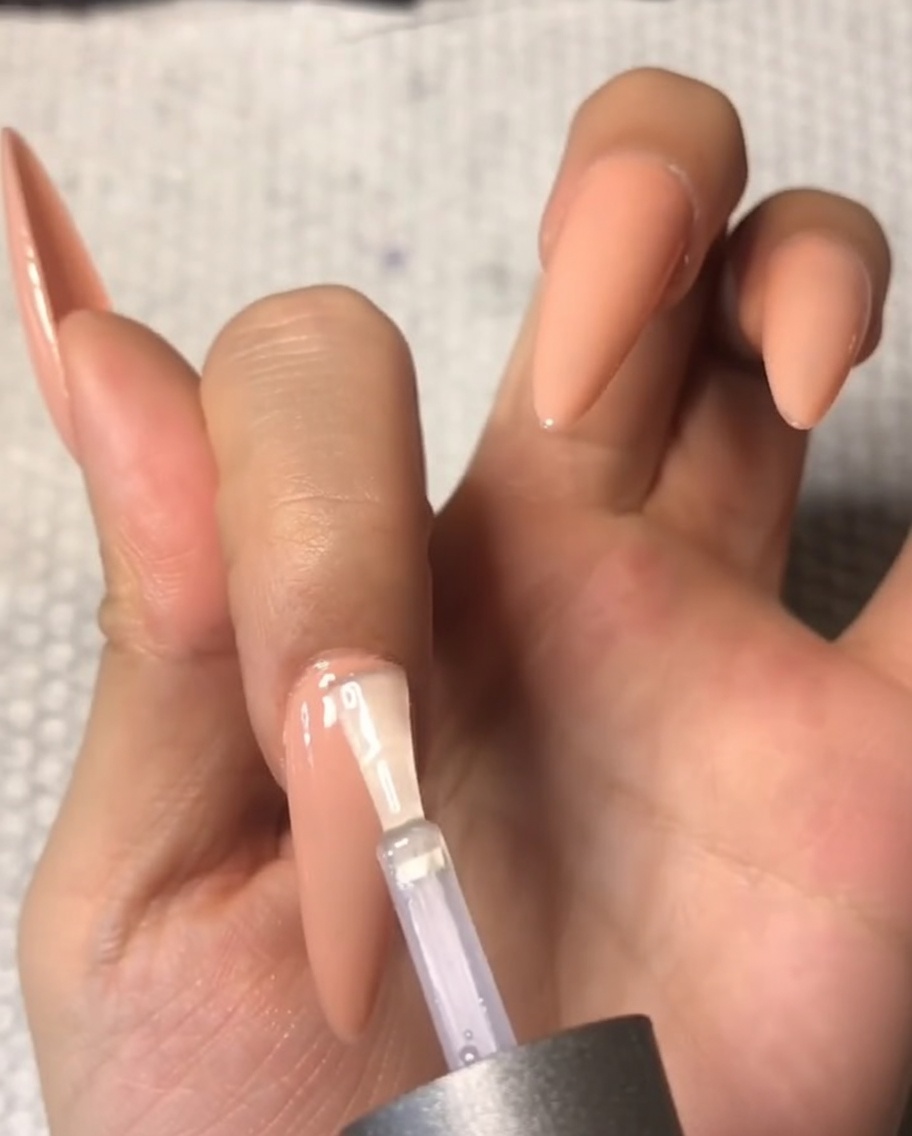 Gros plan sur un pinceau appliquant minutieusement un top coat tempéré transparent près de la zone de la cuticule dun ongle moyen en amande.