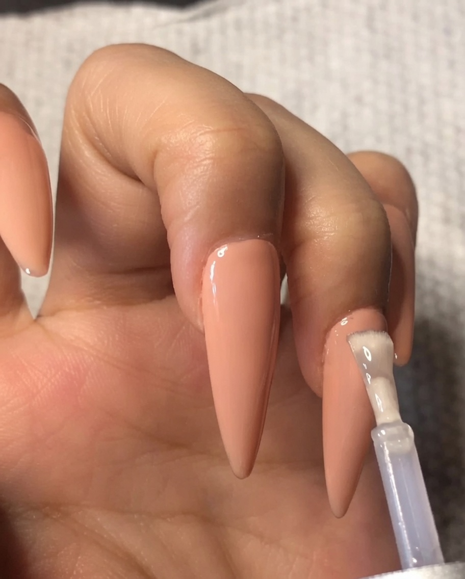 Un pinceau appliquant une couche de top coat gel transparent sur un vernis gel nude sur lannulaire.