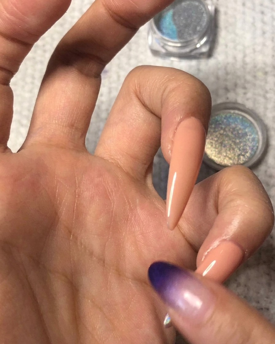 Un doigt propre estompant délicatement le bord de la poudre holographique vers le haut sur longle nude pour créer un dégradé ombré homogène.