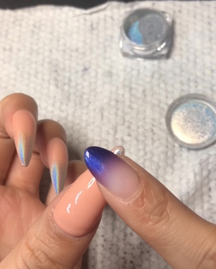 Gros plan dun doigt frottant de la poudre chrome holographique sur le bout dun ongle dauriculaire, créant un dégradé ombré.