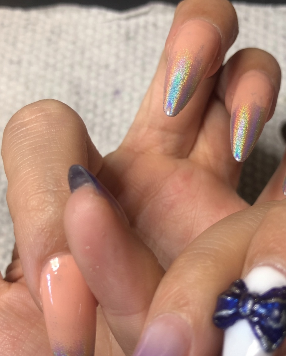 Gros plan dun pinceau appliquant une couche de gel de base sur un index avec un dégradé ombré chrome holographique.