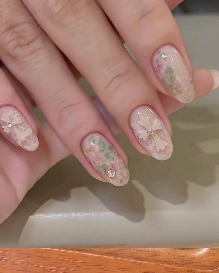 Gros plan dune main retirant le film protecteur dun foil de transfert floral sur un ongle couleur nude.