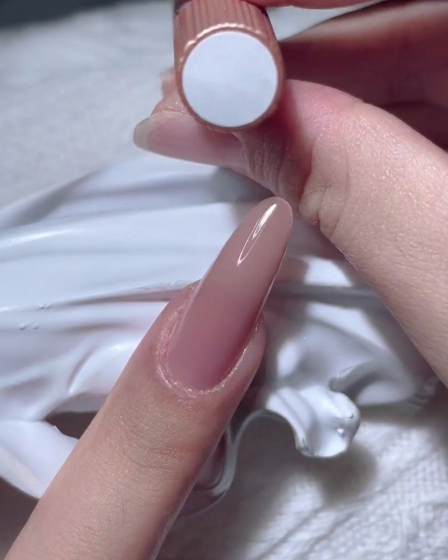 Une main tenant un flacon de vernis gel nude.