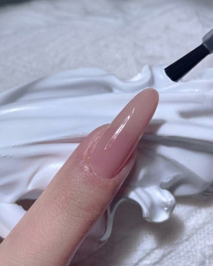 Un pinceau à ongles appliquant un top coat transparent brillant sur un ongle nude.