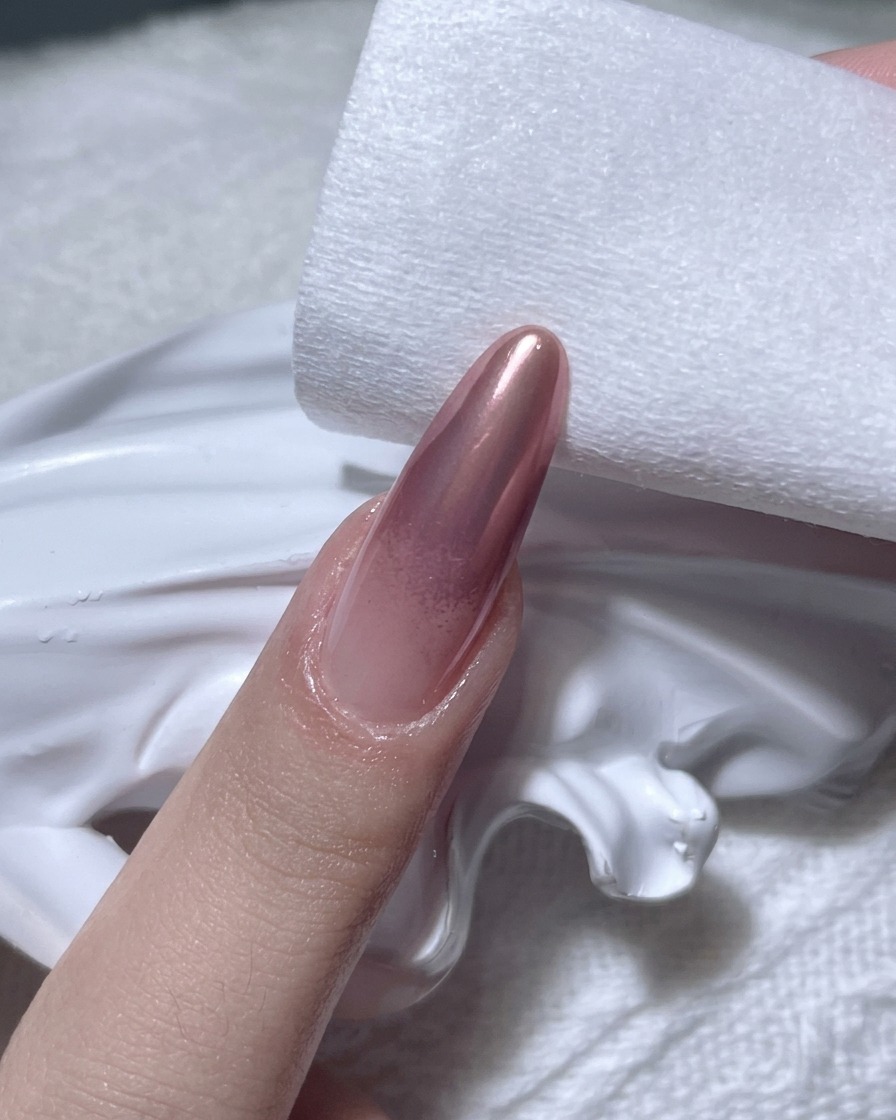 Gros plan dune main utilisant un coton non pelucheux pour essuyer les bords dun ongle au fini chrome or rose.