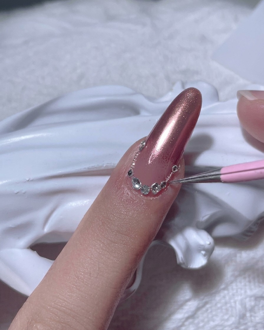 Un outil de précision plaçant un strass transparent sur longle près de la cuticule.