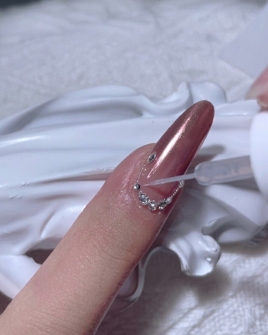 Un arc complet de petits strass transparents disposés le long de la ligne de cuticule dun ongle en chrome or rose.