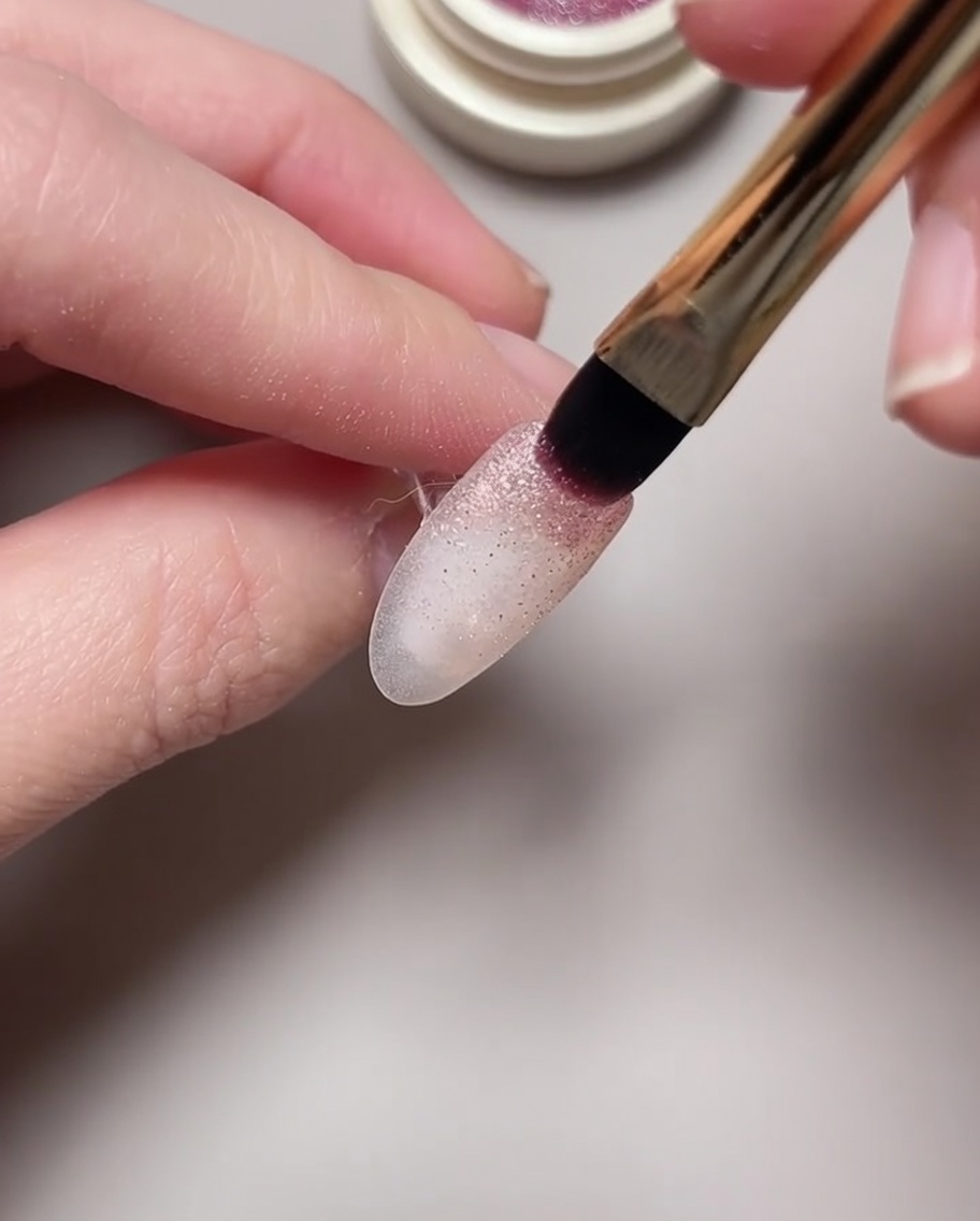 Gros plan dun aimant survolant un vernis gel cat eye humide pour former un motif de nébuleuse.