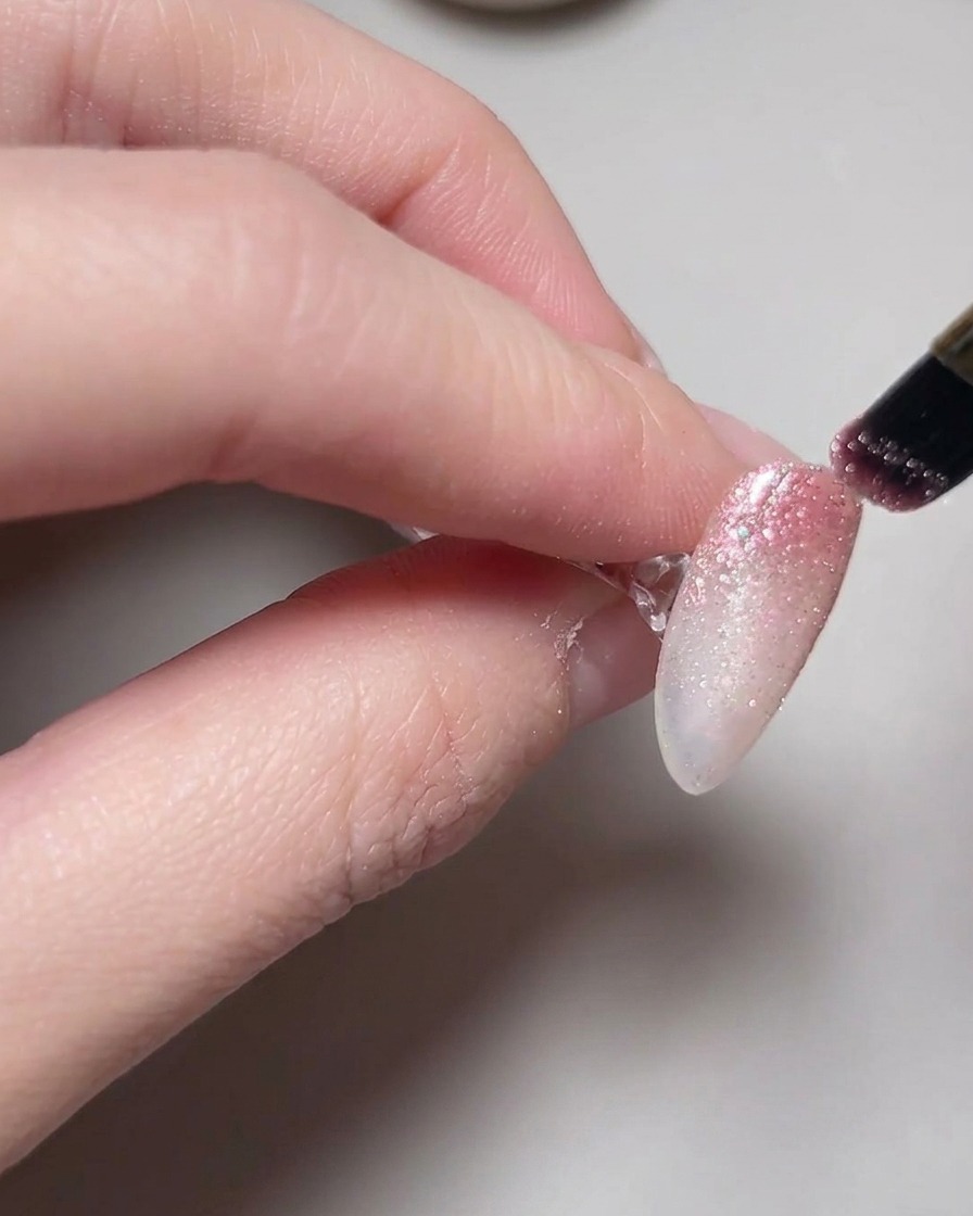 Une main positionnée à lintérieur dune lampe avec le vernis gel cat eye catalysant sur les ongles.