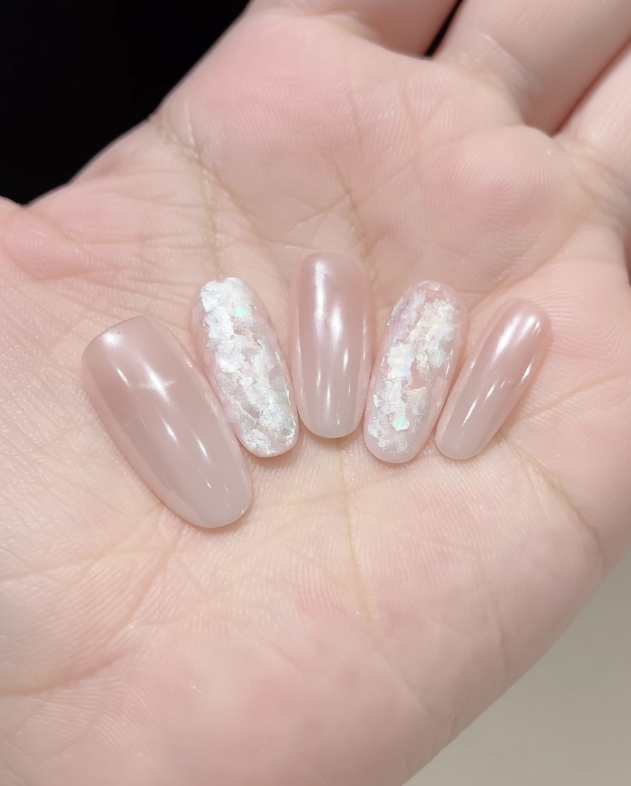 Une pince à épiler ou un pinceau plaçant des éclats de coquillage irisés sur un ongle recouvert de gel.