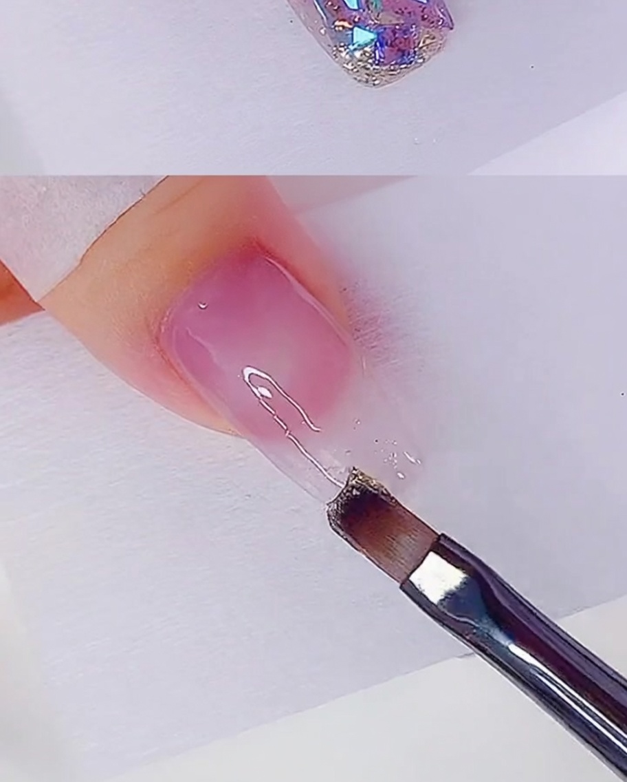 Un pinceau plat appliquant une fine couche de gel pailleté or rose sur le bout dun ongle.