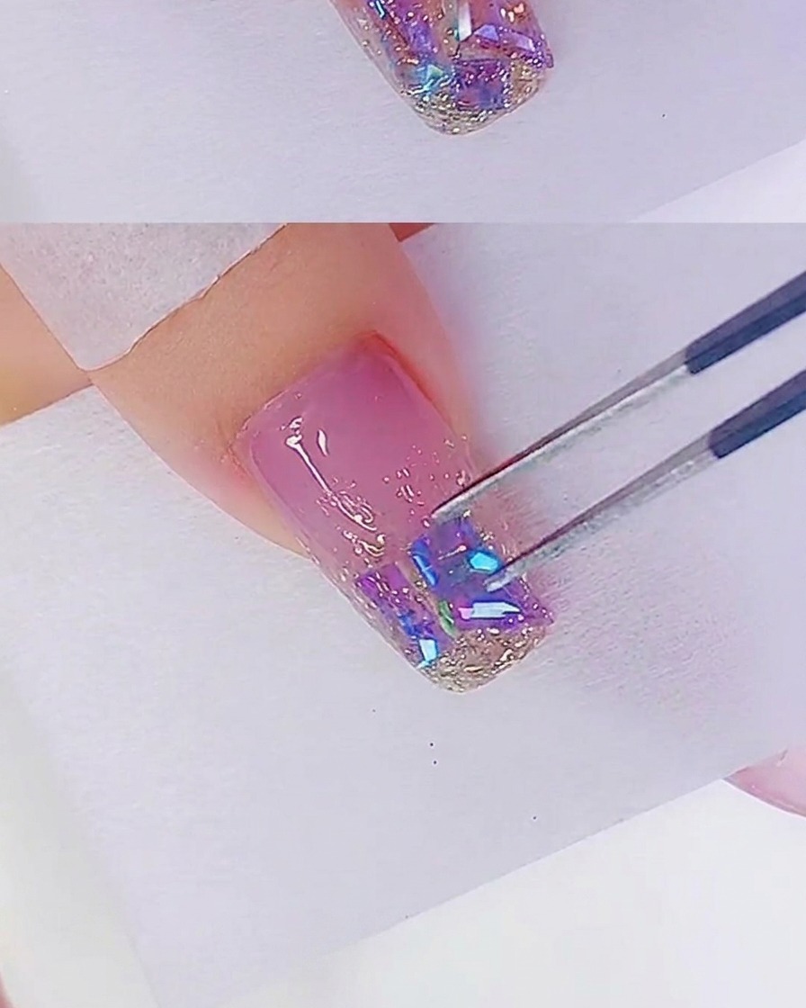 Gros plan dune pince à épiler plaçant des strass iridescents sur le bout dun ongle déjà recouvert de gel pailleté or rose.