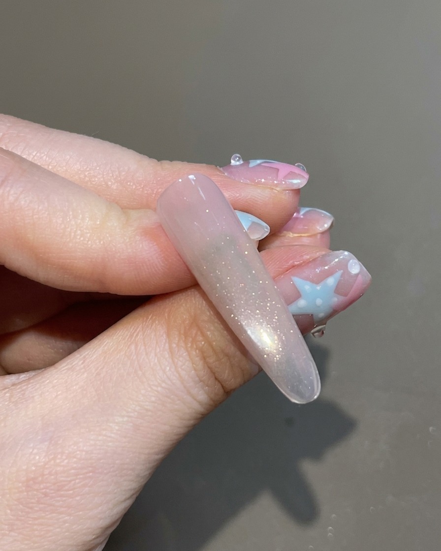 Un pinceau appliquant un top coat transparent sur longle cat-eye entièrement magnétisé et scintillant.