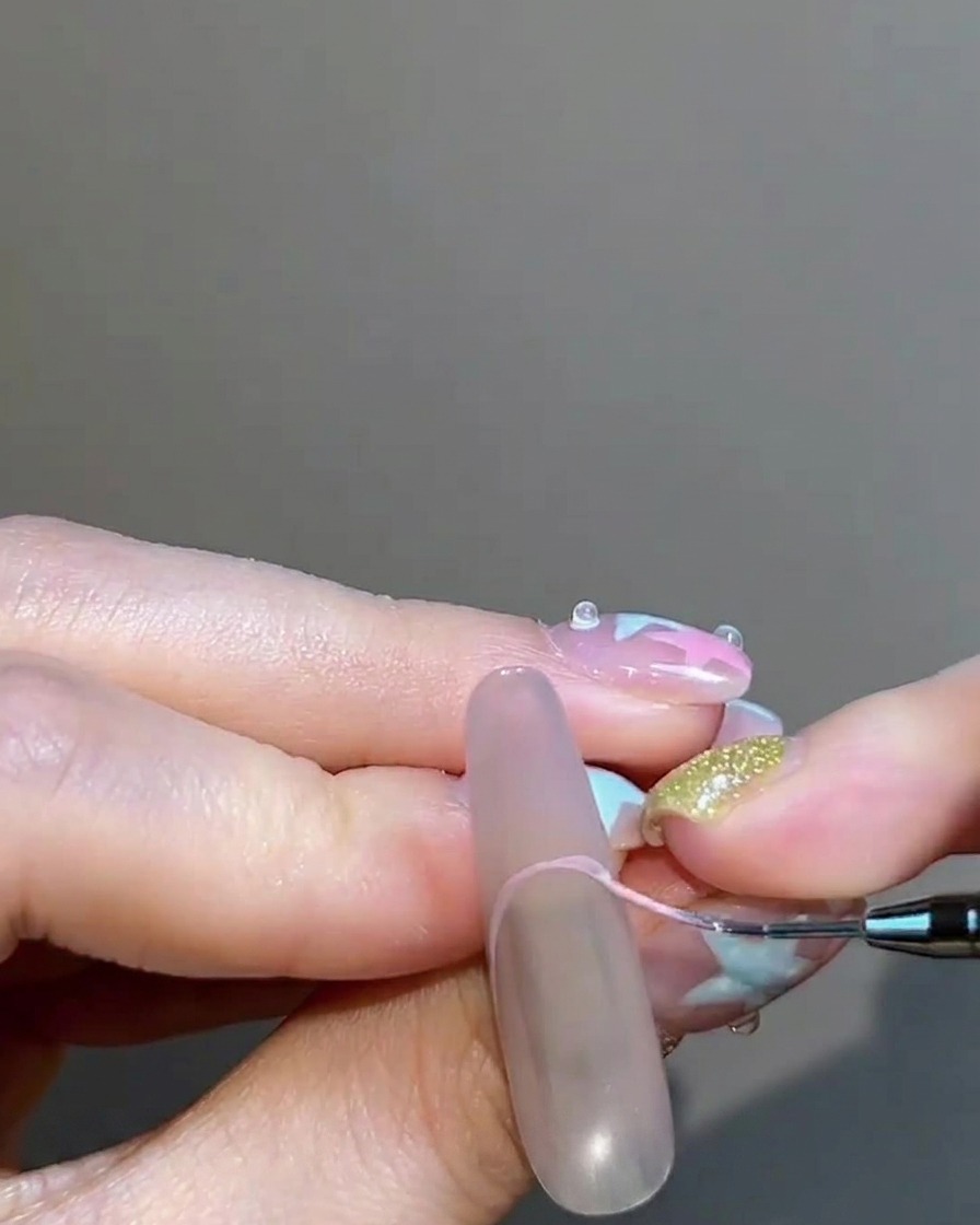 Un pinceau liner fin peignant soigneusement une French avec un gel rose nude sur longle.