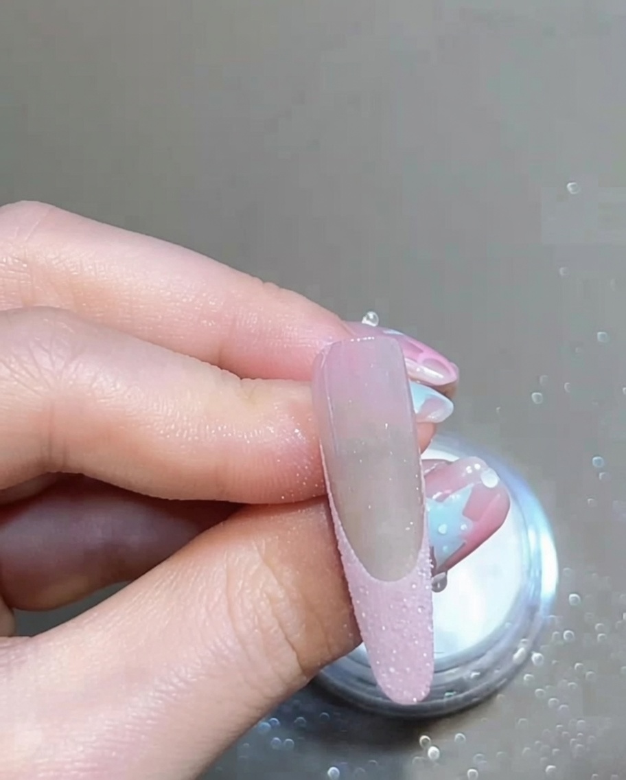 Une brosse douce balayant un ongle manucuré pour éliminer lexcédent de poudre pailletée libre, révélant une French nette.