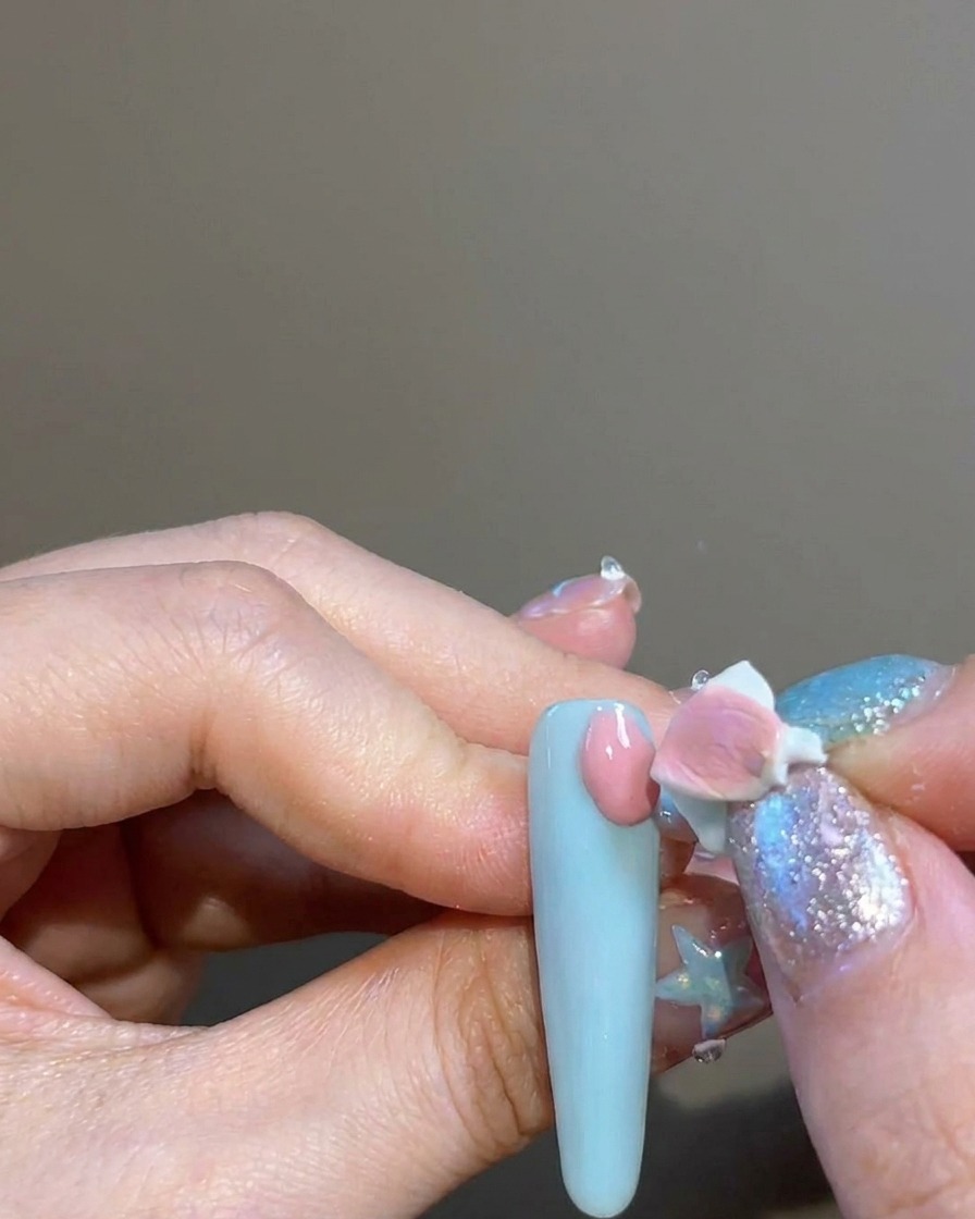Un doigt utilisant un petit applicateur en éponge pour tapoter du pigment rose sur longle autour dun autocollant en forme de croix.