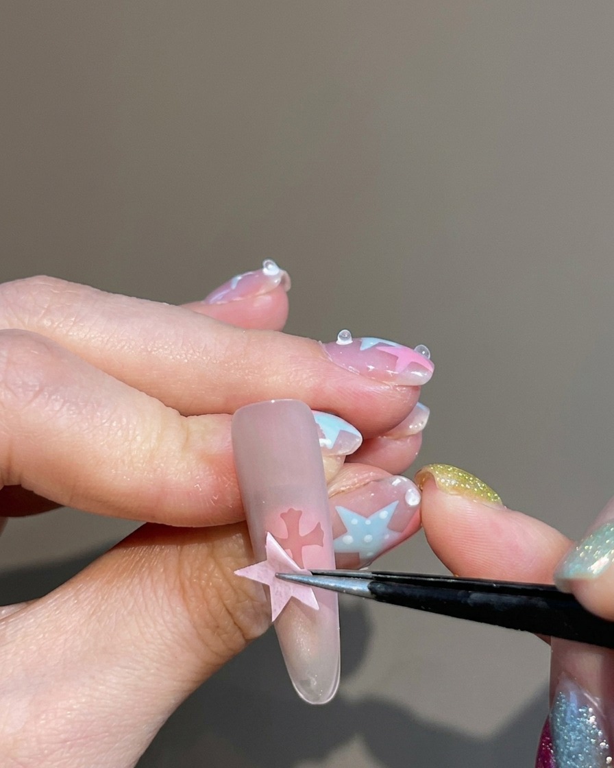 Une pince à épiler décollant un autocollant dun ongle, laissant une silhouette de croix nette au centre de longle teinté de blush.