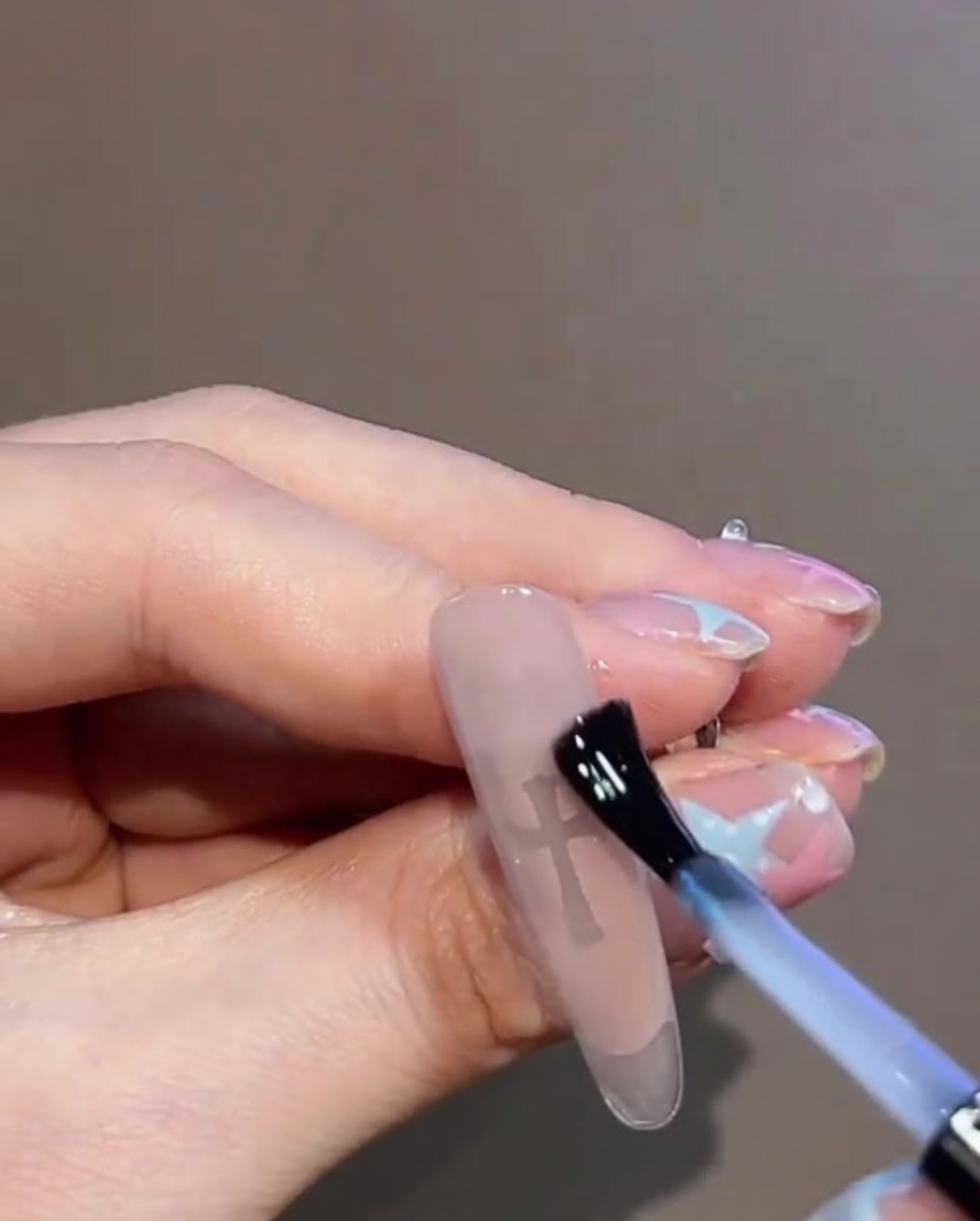 Gros plan dun top coat gel transparent appliqué sur un design dongle terminé présentant un autocollant en croix et des strass.