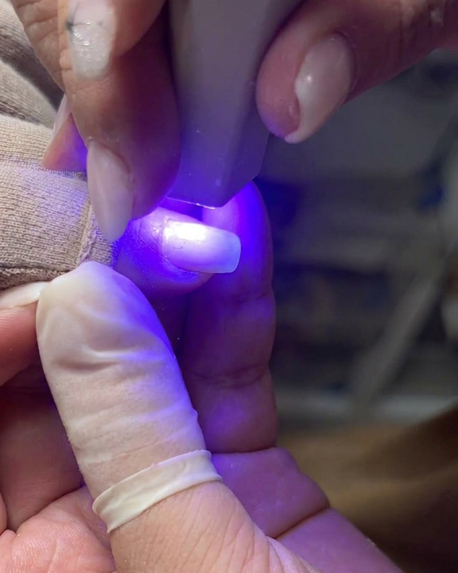 Un pinceau professionnel appliquant une couche uniforme de gel transparent sur un ongle naturel.