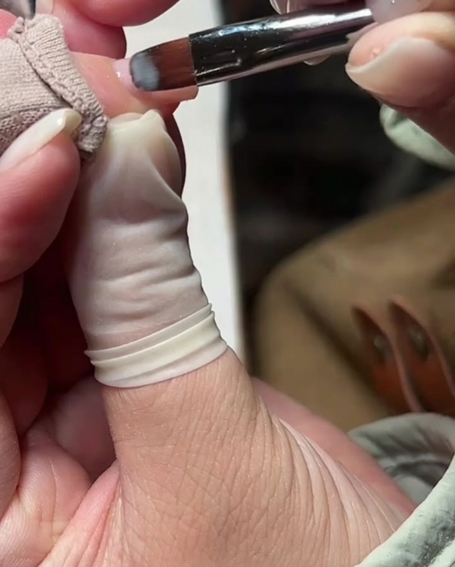 Un pinceau à gel appliquant une fine couche de vernis gel nude laiteux sur longle.