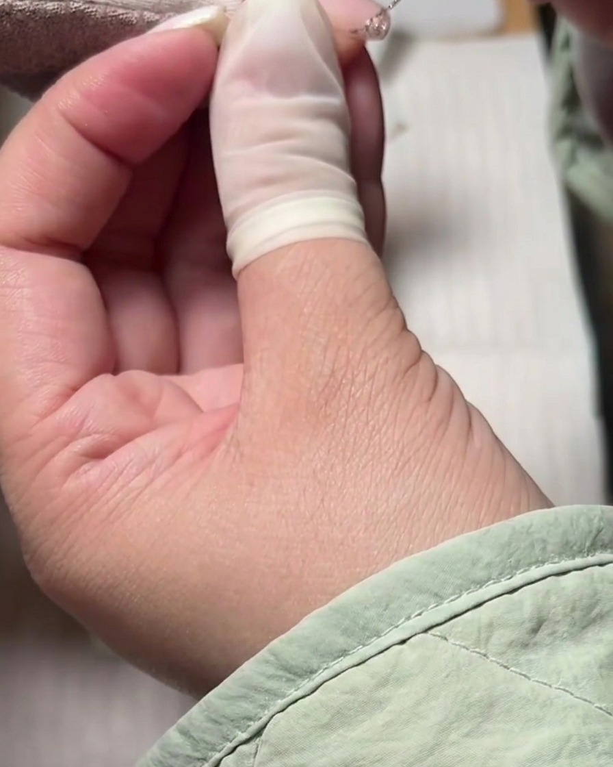 Un pinceau liner créant une ligne de sourire French manucure scintillante en gel argenté sur une base nude.