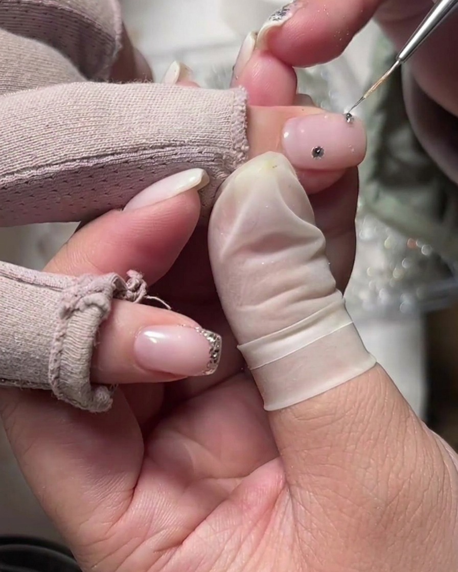 Un outil de précision plaçant un strass unique sur un ongle à base laiteuse près de la cuticule.