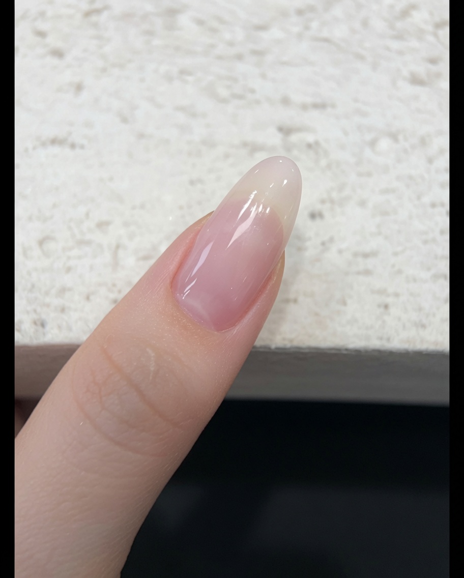 Un pinceau appliquant un vernis gel jelly rose nude translucide sur un ongle naturel.