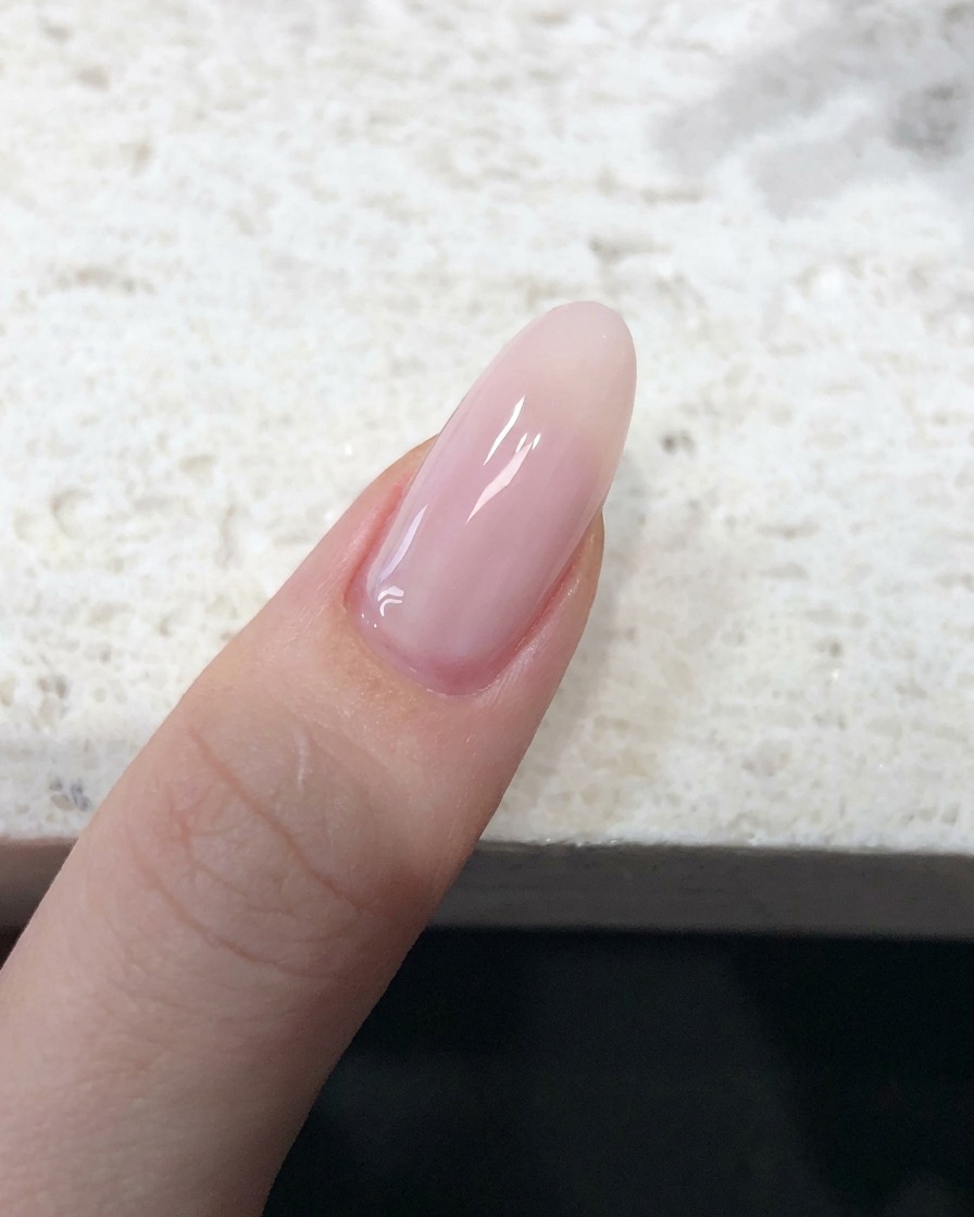 Gros plan sur un ongle recouvert dun vernis jelly rose nude translucide avec un fini lisse.