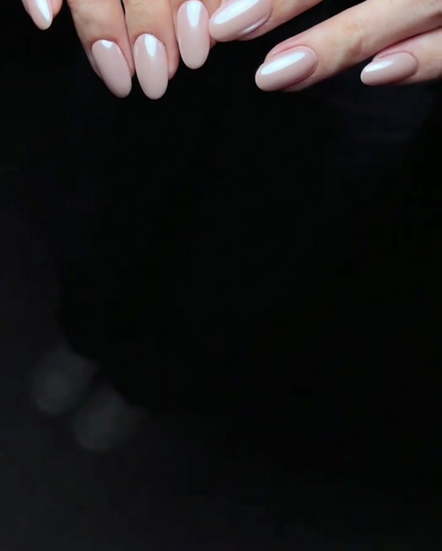 Gros plan dun embout mousse appliquant une poudre nacrée iridescente blanche sur un ongle recouvert de gel rose.