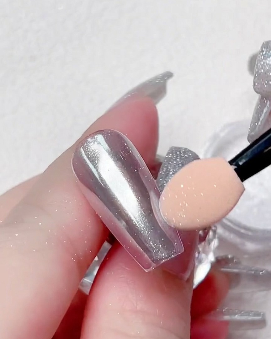 Vue rapprochée dun applicateur polissant la poudre chrome sur les bords dune capsule transparente.