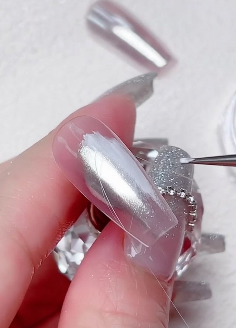 Un pinceau liner dessine des courbes en gel transparent sur longle chromé.