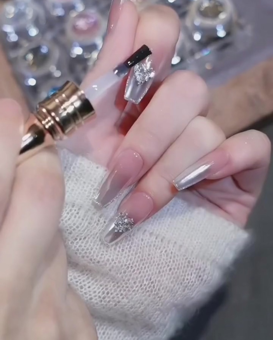 Pinceau top coat contournant soigneusement un charm cœur sur un ongle chromé.