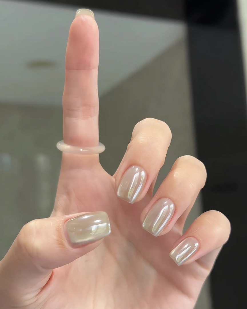 Un pinceau doux lustrant la poudre chrome perlé sur la surface des ongles pour un fini parfaitement lisse.