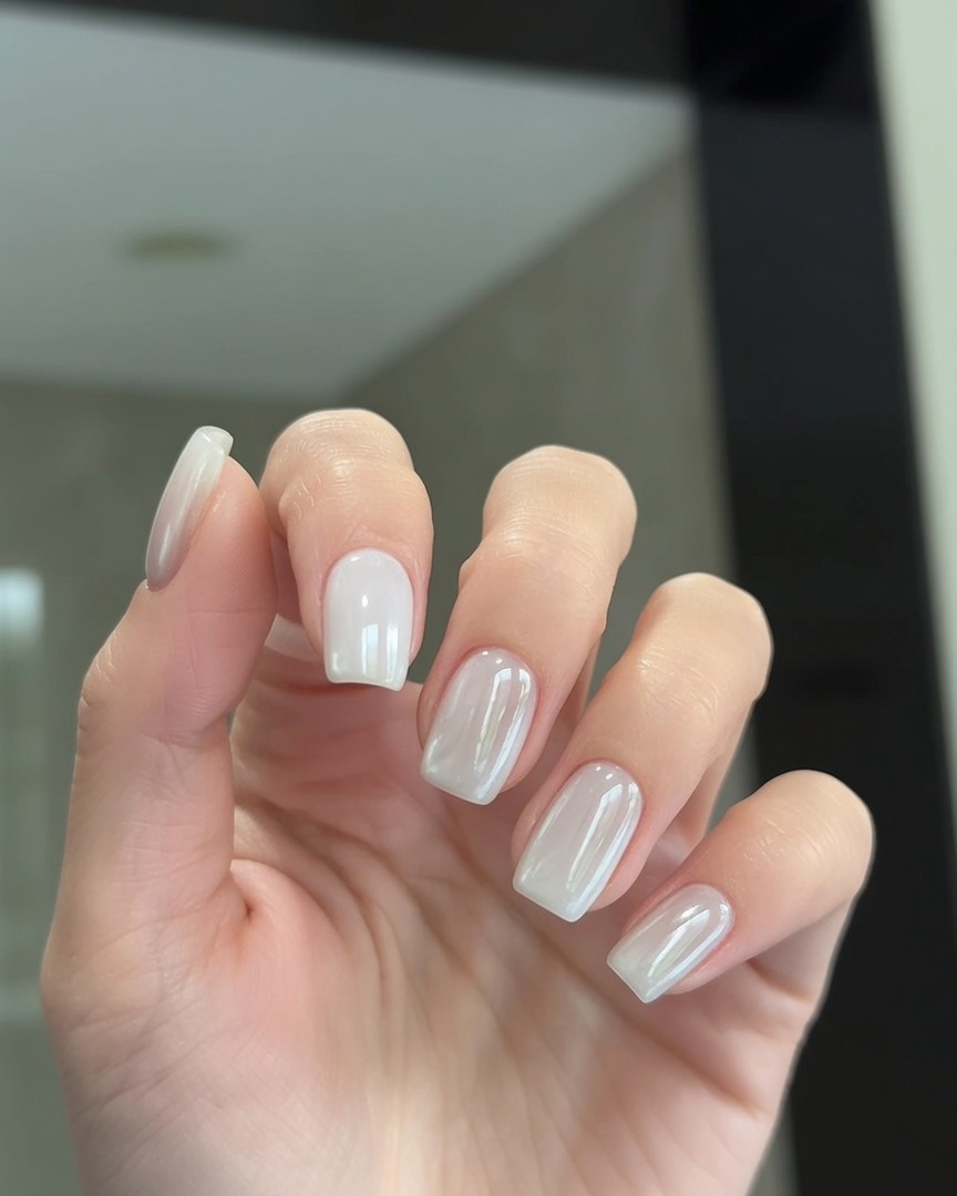 Un pinceau appliquant une fine couche de top coat transparent sur des ongles effet chrome perlé.