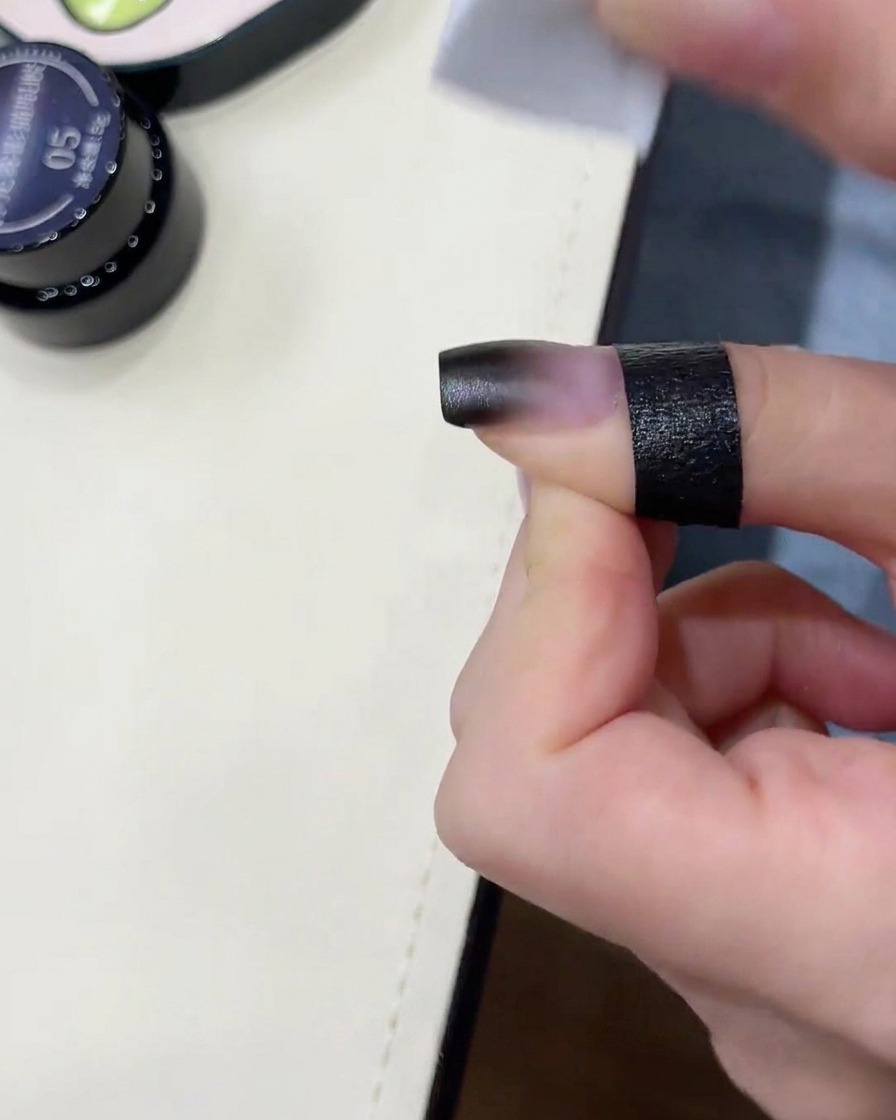 Une éponge estompant du gel noir sur un ongle.