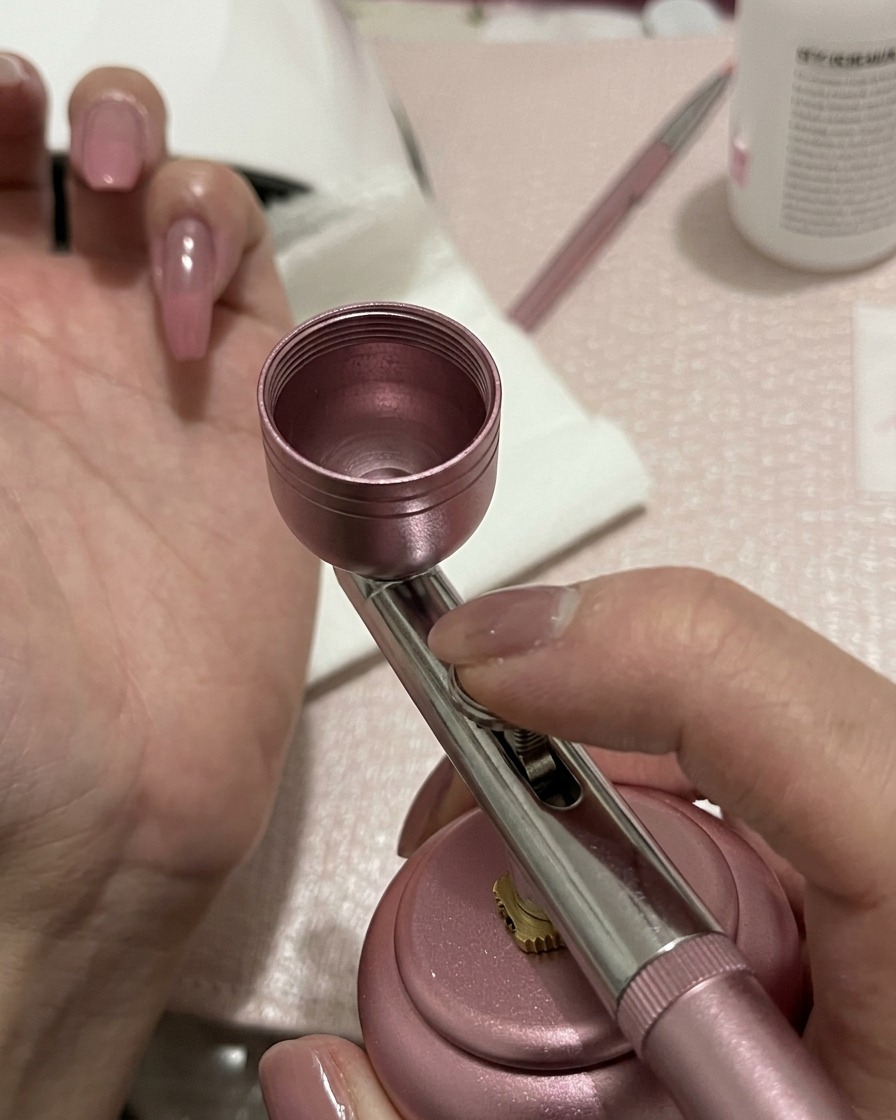 Un aérographe appliquant une légère pulvérisation de gel pêche-rose au centre dun ongle préparé.