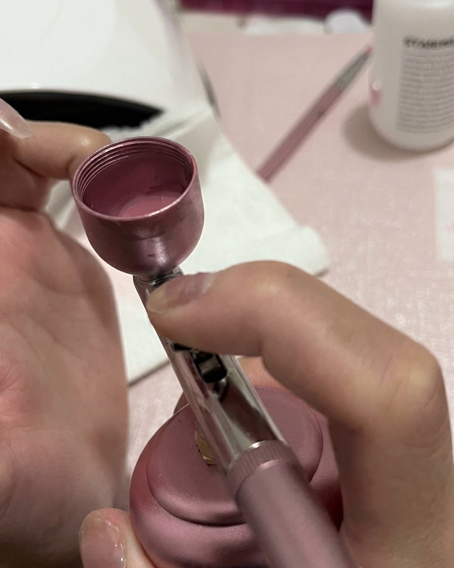 Gros plan dun ongle recevant une pulvérisation plus concentrée de pigment rose à la base et sur la section médiane.