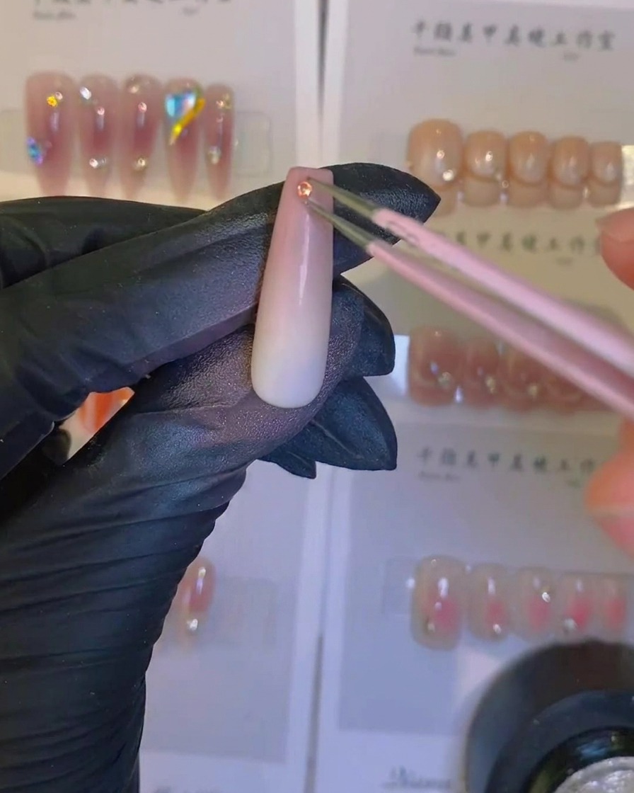 Un pinceau appliquant un top coat transparent brillant sur un ongle ombré à laérographe avec un cristal.