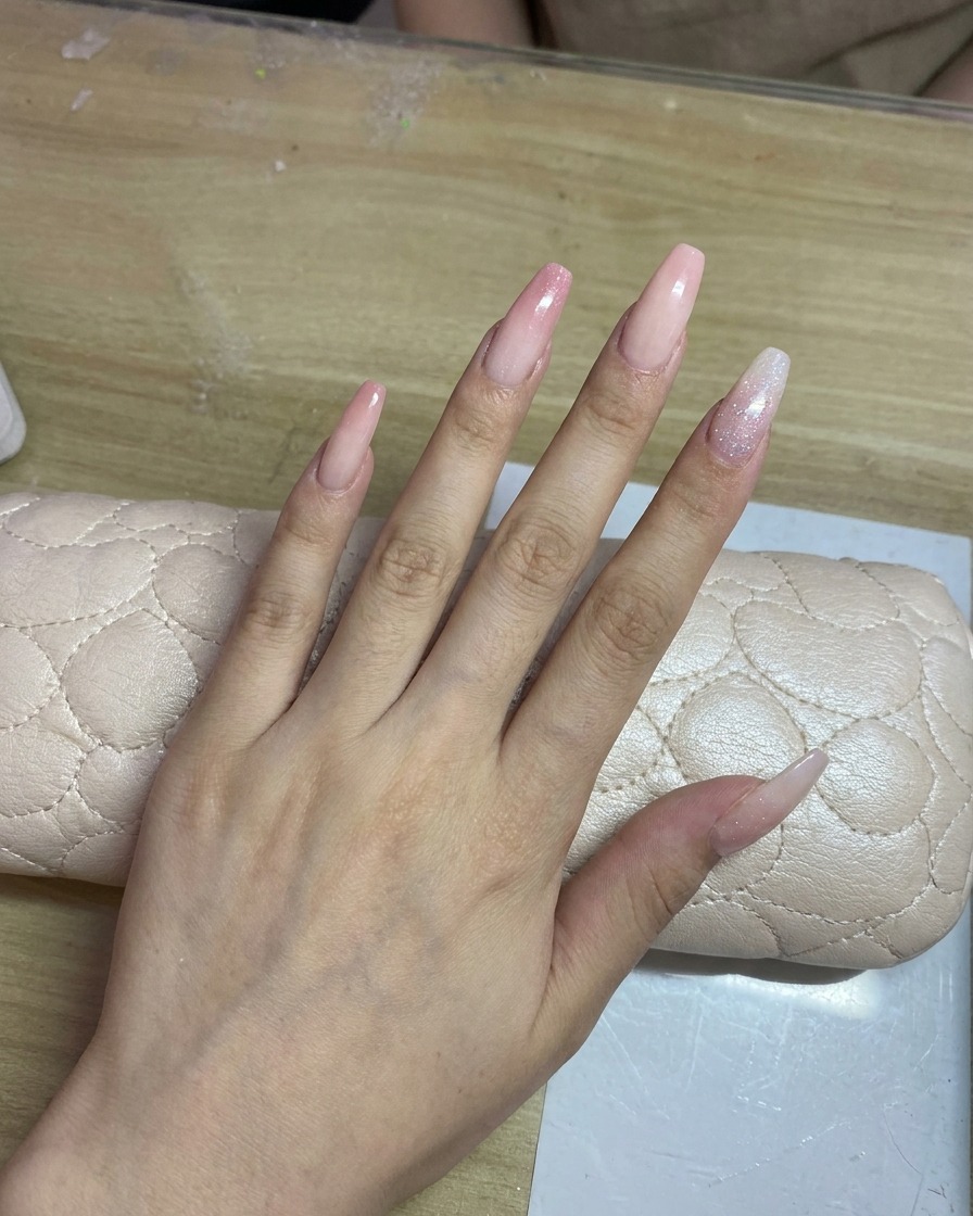 Une main avec de longs ongles clairs étant aérografée avec un délicat dégradé rose.