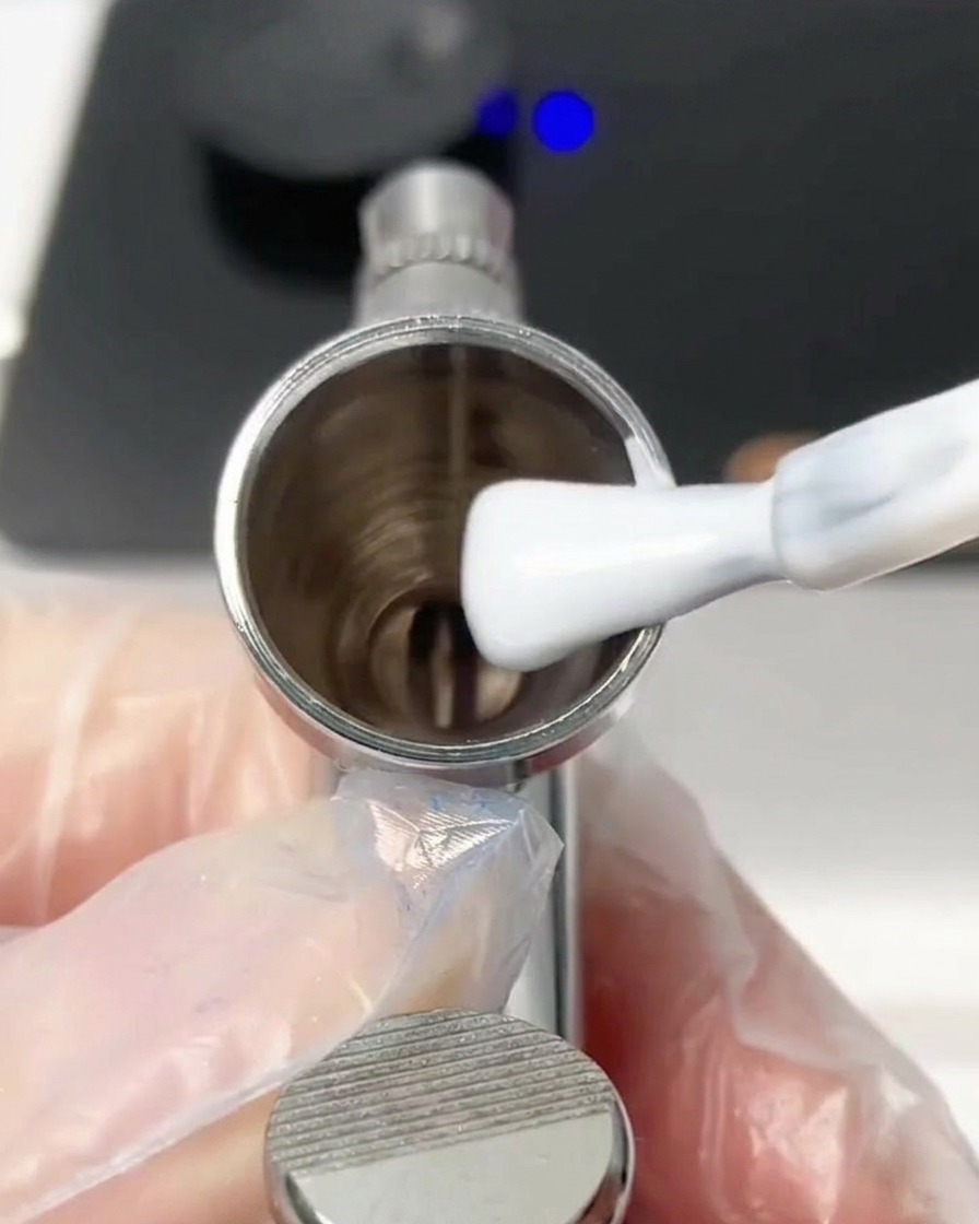 Un pinceau déposant une goutte de vernis gel blanc dans le godet métallique de laérographe.