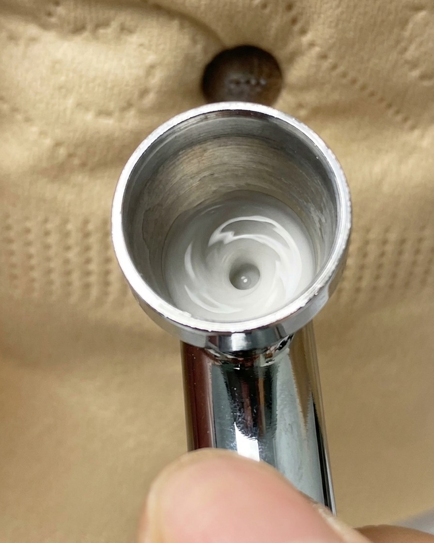 Un aérographe vaporisant une fine brume de pigment blanc sur une capsule partiellement recouverte dadhésif.
