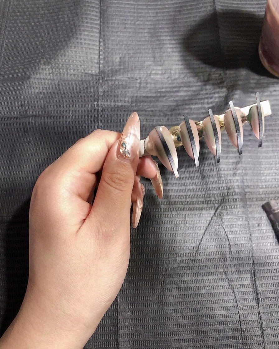 Pistolet à aérographe pulvérisant une fine couche de gel blanc sur des faux ongles sur support.