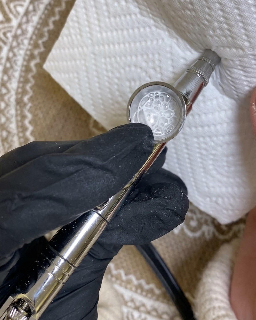 Un aérographe dirigé vers un essuie-tout, montrant un motif de test en peinture blanche.