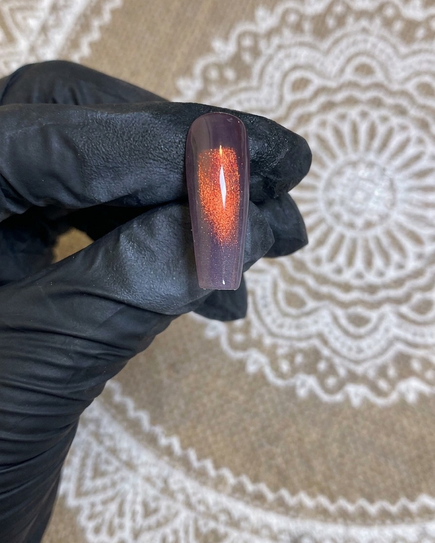 Gros plan sur la buse de laérographe pulvérisant un dégradé blanc sur un ongle à base sombre.