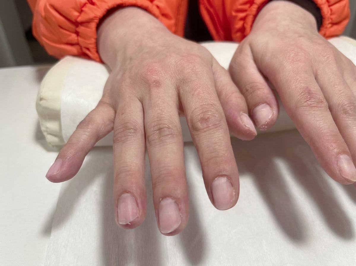 Vue rapprochée de deux mains aux ongles en gel transparents, posées sur un coussin de salon blanc.