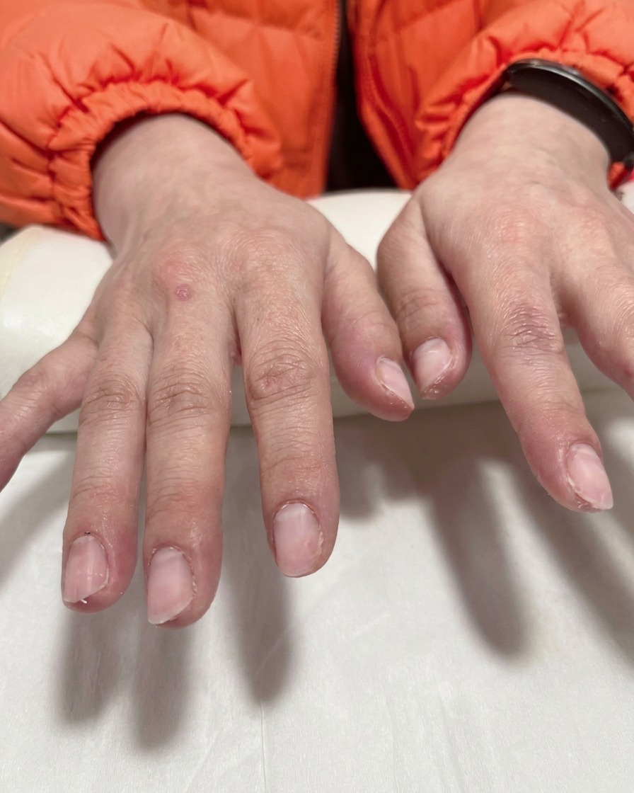 Gros plan sur un aérographe pulvérisant une fine brume blanche sur les pointes des ongles recouverts de pochoirs violets.