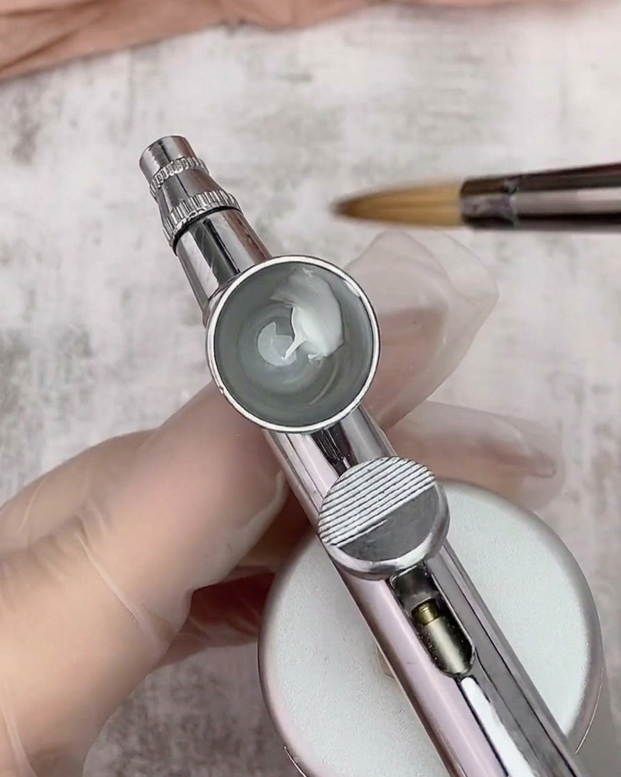 Gros plan à lintérieur dun godet contenant un mélange de gel blanc et de diluant, avec un pinceau en arrière-plan.